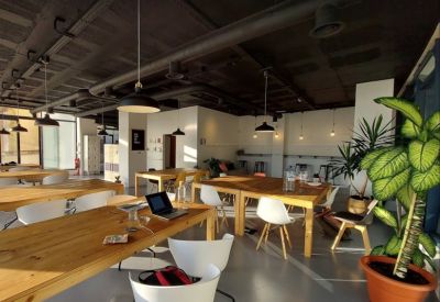 Open-plan workspace with long timber desks, white chairs, and industrial ceiling pipes.