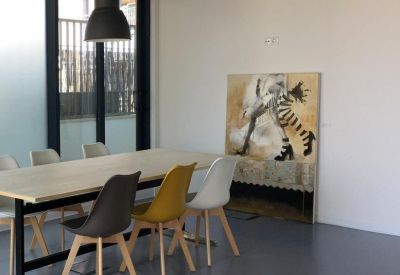 Modern meeting room with a light wood table, grey and yellow chairs, and abstract wall art.