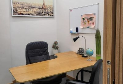 Private office with a light wood L-shaped desk, whiteboard, and framed art of Paris.
