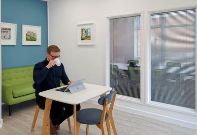 Bright breakout space with a green sofa, blue feature wall, and small cafe table.