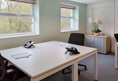 Private office suite with two white desks and large windows overlooking trees.