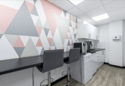 Modern communal kitchen and breakout area with pink geometric wall art.