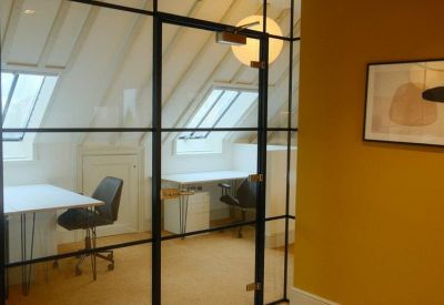 Glass-walled office suite with white desks and sloped ceilings.