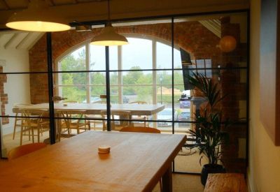 Meeting room seen through a glass partition featuring a long wooden table and greenery.