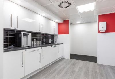 Modern communal kitchen with sleek white cabinetry, black splashback, and vibrant red feature walls.
