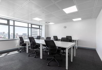 Bright open-plan workspace with white desks, ergonomic black chairs, and large windows.