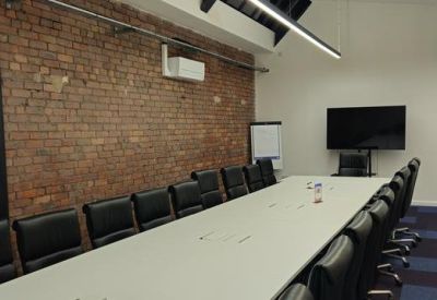 Boardroom with a long white table and exposed brick feature wall.