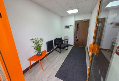 Waiting area with a modern orange table, green plant, and black chair.