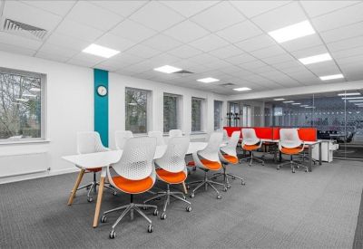 Spacious coworking area with long white tables, orange-accented chairs, and a teal feature wall.