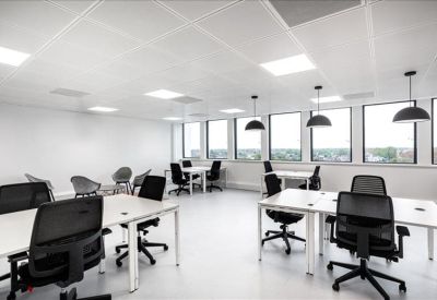 Open-plan coworking space with white desks and black ergonomic chairs under bright panel lighting.