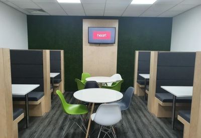 Communal breakout area with high-backed booths, round tables, and a green feature wall with a TV.