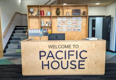 Wooden reception desk with the words Welcome to Pacific House and a staircase in the background.