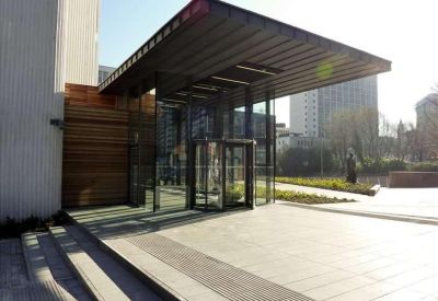 Modern glass entrance with a revolving door under a large dark metal canopy.