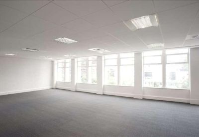 Spacious, open-plan office space with grey carpeting and large windows providing natural light.