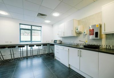 Modern staff kitchen area with white cabinetry, black countertops, and breakfast bar seating.