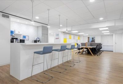 Communal break area with a white breakfast bar, blue high stools, and a kitchen facility.