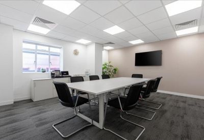Spacious meeting room with a large white table, black chairs, and a wall-mounted screen.