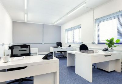 Bright open-plan office space featuring white desks and blue carpeting.