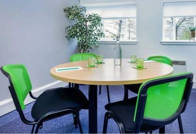 Modern meeting room with a round wooden table and vibrant green chairs.