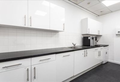 Sleek white communal kitchen area with dark countertops.