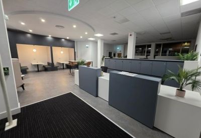Spacious reception area with grey front desks, potted plants, and modern seating booths in the background.