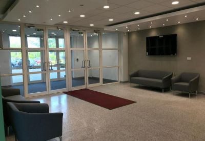 Reception lobby with grey seating, glass doors, and a wall-mounted television.
