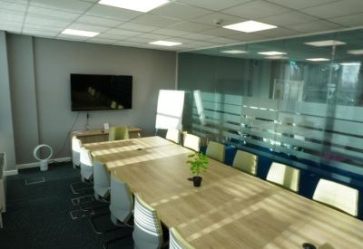 Professional meeting room featuring a long light-wood table and grey upholstered chairs.