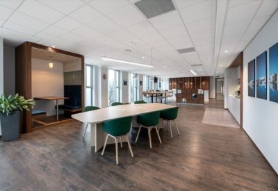Modern communal area with wood flooring, a long table with green chairs, and a private wooden booth.