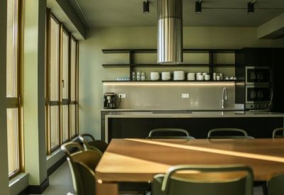 Modern office kitchen area with dark cabinetry, wooden table, and sleek pendant lighting.