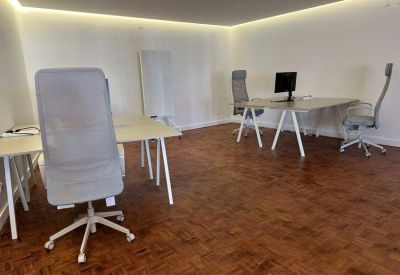 Bright open-plan office with white desks, grey ergonomic chairs, and parquet flooring.