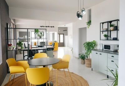 Dining and breakout area with yellow chairs, a round table, and a kitchen unit.
