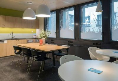 Communal break area at Rue de la Cité 1 with a wooden dining table, modern pendant lights, and kitchen cabinets.