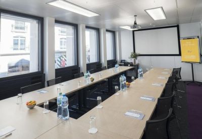 Spacious boardroom with a large U-shaped table, water bottles, and a projector screen.