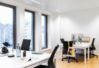 Minimalist open-plan office with white desks, ergonomic black chairs, and light wood flooring.