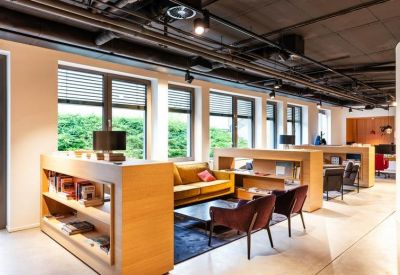 Bright break area with wooden shelving, a yellow sofa, and dark leather armchairs under exposed ceilings.
