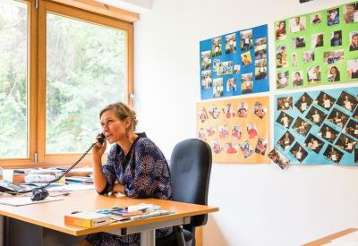 Woman at a desk talking on a vintage telephone in a bright office.