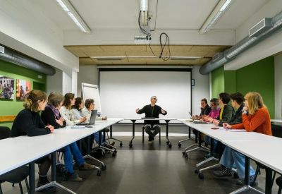 A formal meeting room with people seated around a U-shaped white table.