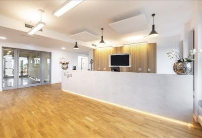 Bright reception lobby featuring a long white desk and warm wooden flooring.