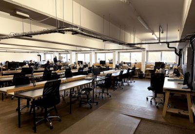 Large open-plan office with rows of long desks and black ergonomic chairs.