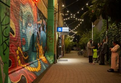 Vibrant outdoor alleyway at night with colorful wall murals and hanging string lights.