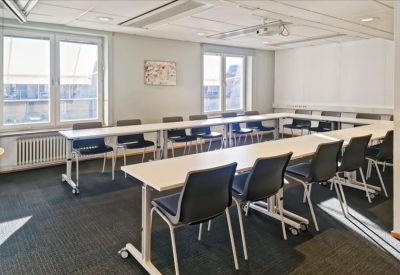 Flexible workspace area with several round wooden tables and grey carpeting.