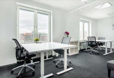 Spacious open-plan office with white height-adjustable desks and ergonomic chairs.