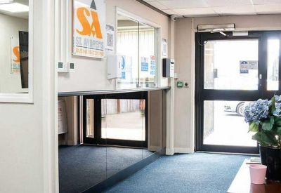 Bright reception lobby with blue carpeting, glass partitions, and floral arrangements.