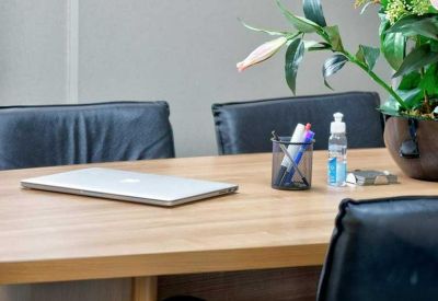 Close-up of a wooden conference table with a laptop, stationery, and a potted plant.
