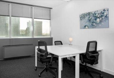 Bright four-person office with white desks and modern abstract wall art.