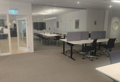 Modern open-plan workspace featuring several desks with gray privacy screens and a glass-walled meeting room.