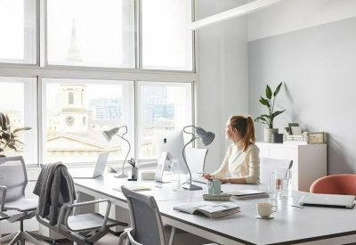 Sunlit open-plan office with white desks, ergonomic chairs, and large windows.