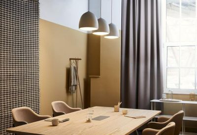 Modern meeting room with a wooden table, tan chairs, and three large pendant lights.