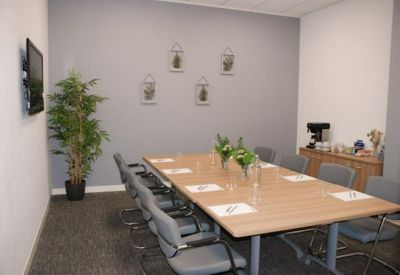 Professional boardroom with a long wooden table, grey chairs, and a wall-mounted television.