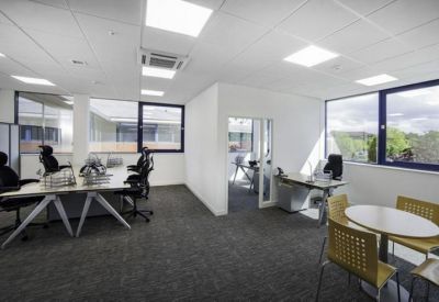 Spacious open-plan office with modern white desks, ergonomic chairs, and large windows.